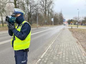 zdjęcie kolorowe:  policjant wydziału ruchu drogowego mierzący prędkość pojazdu w rejonie oznakowanego przejścia dla pieszych