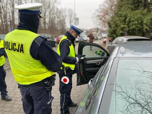 zdjęcie kolorowe: dwóch policjantów katowickiej drogówki stojących przy samochodzie osobowym zatrzymanym do kontroli