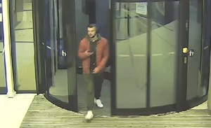 zdjęcie kolorowe: mężczyzna ubrany w czerwona kurtkę, ciemne spodnie i białe buty wchodzący przed drzwi obrotowe do galerii