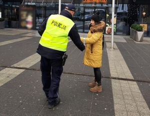 zdjęcie kolorowe: funkcjonariusz Policji podczas działań "Błyśnij dla życia" wręczający elementy odblaskowe kobiecie