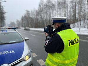 zdjęcie kolorowe: policjant katowickiej drogówki wykonujący pomiar prędkości pojazdu, stojący koło radiowozu
