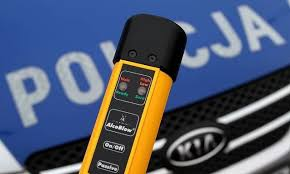 zdjęcie kolorowe: na tle policyjnego radiowozu urządzenie do badania stany trzeźwości kierujących
