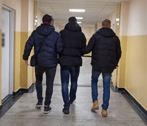 zdjęcie kolorowe: policjanci wydziału kryminalnego prowadzący korytarzem zatrzymanego mężczyznę