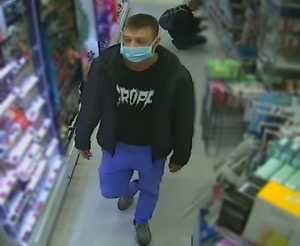 zdjęcie kolorowe: zdjęcie kolorowe: mężczyzna w sklepie kosmetycznym ubrany w niebieskie spodnie, czarną koszulkę z białym napisem i czarna kurtkę z maseczką ochronna na twarzy,