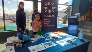 zdjęcie kolorowe: dwie policjantki katowickiej komendy i dziecko na stoisku profilaktycznym