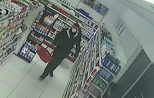 zdjęcie kolorowe: zrzut z nagrania kamer monitoringu sklepowego przedstawiający mężczyznę ubranego w ciemne spodnie, ciemna kurtkę i maseczkę ochronna założoną na twarz spacerującego w sklepie z koszykiem w ręce