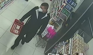 zdjęcie kolorowe: zrzut z nagrania kamer monitoringu sklepowego przedstawiający mężczyznę ubranego w ciemne spodnie, ciemna kurtkę i maseczkę ochronna założoną na twarz spacerującego w sklepie z koszykiem w ręce