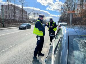 zdjęcie kolorowe: dwóch policjantów wydziału ruchu drogowego rozmawiający z kierującym samochodu osobowego