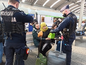 zdjęcie kolorowe: policjanci katowickiego oddziału prewencji rozdający jedzenie oczekującym na peronie uchdźcom
