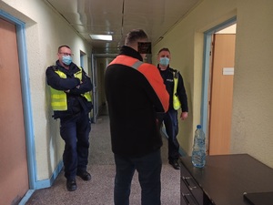 zdjęcie kolorowe: dwóch policjantów katowickiej drogówki stojący na korytarzu z mężczyzną, który został zatrzymany za wręczenie łapówki