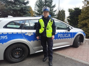 zdjęcie kolorowe: posterunkowa Aleksandra Trzaska stojąca w mundurze przez policyjnym radiowozem
