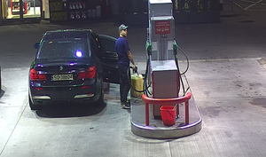 zdjęcie kolorowe: młody mężczyzna ubrany w granatowe spodnie, ciemne buty sportowe, granatowa koszulkę z krótkim rękawem z emblematem tarczy Kapitana Ameryki wysiadający z granatowego BMW