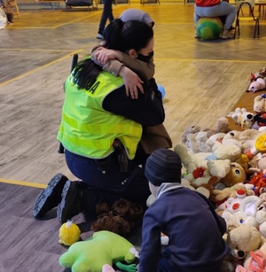 zdjęcie kolorowe: policjantka katowickiej drogówki przytulająca małą dziewczynkę na sali gimnastycznej