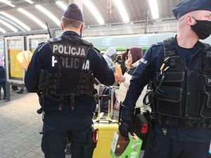 zdjęcie kolorowe: dwóch umundurowanych policjantów na peronie rozdający jedzenie uchodźcom