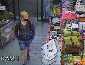 zdjęcie kolorowe: młody mężczyzna w sklepie spożywczym ubrany w niebieskie jeansowe spodenki, granatowa bluzę zapinaną na zamek i ciemna maseczkę ochronną na twarzy