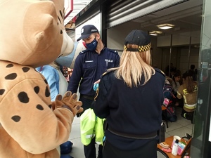zdjęcie kolorowe: maskotka Rysiu, policjant i strażniczka miejska przed pokojem dla matek z dziećmi