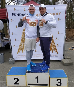 zdjęcie kolorowe: dzielnicowy Komisariatu III Policji w Katowicach sierżant sztabowy Kamil Sierny i dzielnicowy Komisariatu IV Policji w Katowicach sierżant sztabowy Łukasz Słabik w strojach sportowych na stopniach podium podczas VII Biegu Śląskich Aniołów