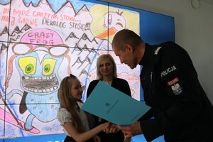 zdjęcie kolorowe: policjant wręczający dziewczynce nagrodę za udział w konkursie "Śnieżny dekalog"