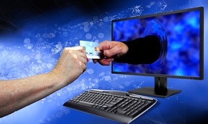 zdjęcie kolorowe: grafika przedstawiająca komputer stacjonarny, gdzie z monitora wystaje ręka sięgająca po kartę bankomatowa podawaną przez kobieca rękę