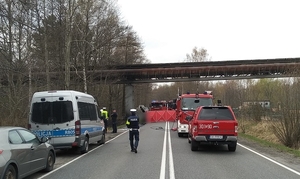 zdjęcie kolorowe: droga na której doszło do śmiertelnego wypadku drogowego, z pojazdami służbowymi Policji i Straży Miejskiej. Na środku jezdni policjant wykonujący czynności