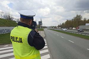 Zdjęcie kolorowe przedstawia policjanta mierzącego prędkość pojazdów.