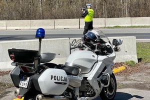 Zdjęcie kolorowe przedstawia policjanta mierzącego prędkość pojazdów oraz motocykl policyjny.