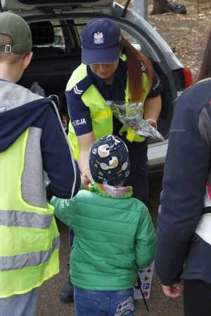 zdjęcie kolorowe:  policjantka katowickiej komendy rozdająca materiały profilaktyczne i odblaski dzieciom