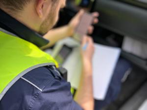 zdjęcie kolorowe: policjant katowickiej drogówki siedzący w radiowozie, który sporządza dokumentację z kontroli drogowej