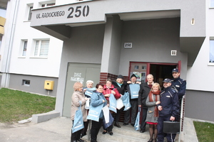 zdjęcie kolorowe: katowiccy policjanci z grupą seniorów stojących przed wejściem do bloku mieszkalnego