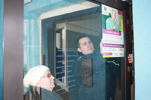 zdjęcie kolorowe: policjant zawieszający z seniorką plakat na drzwiach klatki schodowej