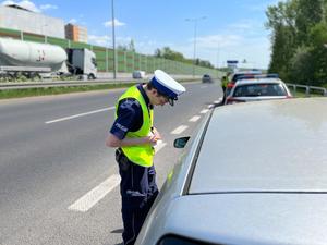 zdjęcie kolorowe: policjant katowickiej drogówki stojący obok samochodu osobowego