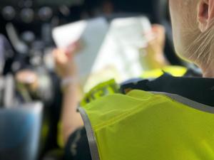 zdjęcie kolorowe: ramie policjanta siedzącego w radiowozie, który wypełnia dokumentację z kontroli drogowej