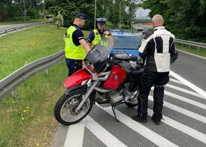 zdjęcie kolorowe: dwóch policjantów ruchu drogowego rozmawiający z kierującym motocyklem, który został zatrzymany do kontroli drogowej