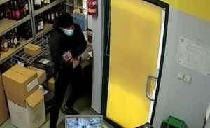 zdjęcie kolorowe: mężczyzna ubrany w czarne spodnie, czarna kurtkę i czarną czapkę z maseczka ochronną na twarzy w pokoju socjalnym sklepu spożywczego