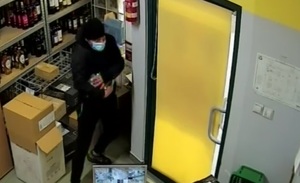 zdjęcie kolorowe: mężczyzna ubrany w czarne spodnie, czarna kurtkę i czarną czapkę z maseczka ochronną na twarzy w pokoju socjalnym sklepu spożywczego