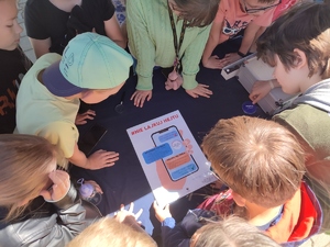 zdjęcie kolorowe: dzieci zgromadzone wokół stołu, które oglądają plakat promujący bezpieczne zachowania w Internecie