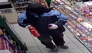 zdjęcie kolorowe: mężczyzna ubrany w czarne spodnie, ciemne buty sportowe, czarno-niebieska kurtkę, z czarnym swetrem na głowie zasłaniającym twarz, w białych ogrodniczych rękawiczkach trzymający gaśnice w ręce