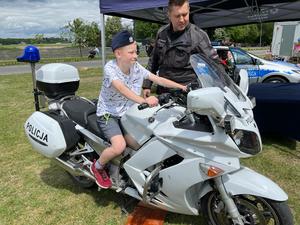 zdjęcie kolorowe: policjant katowickiej drogówki stojący przy motorze i rozmawiający z chłopcem, który siedzi na motorze służbowym