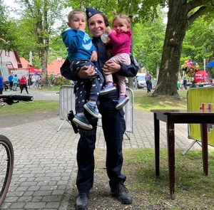 zdjęcie kolorowe: policjantka z dwójka dzieci, które trzyma na rękach podczas pamiątkowego zdjęcia