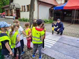 Zdjęcie kolorowe: policjant z dziećmi które uczą się przechodzić prawidłowo przez przejście dla pieszych