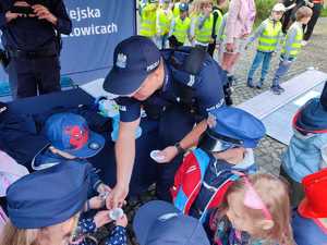 Zdjęcie kolorowe: policjant i dzieci na stanowisku profilaktycznym  rozmawiający o bezpieczeństwie w ruchu drogowym
