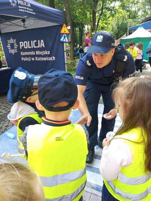 Zdjęcie kolorowe: policjant rozdający dzieciom „medale” za udział w konkursach