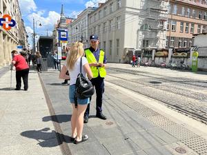 zdjęcie kolorowe: policjant rozmawiający na chodniku w centrum miasta z pieszą o bezpieczeństwie w ruchu drogowym