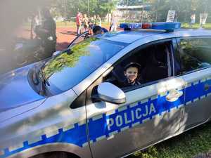 zdjęcie kolorowe: dziecko które siedzi za kierownica policyjnego radiowozu