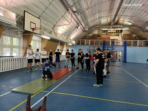 zdjęcie kolorowe: sala gimnastyczna - policyjny instruktor omawiający poprawność wykonania ćwiczenia uczniom klas mundurowych