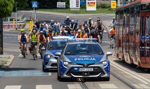 zdjęcie kolorowe?: policjanci drogówki w dwóch radiowozach pilotujący kolarzy biorących udział w przejeździe