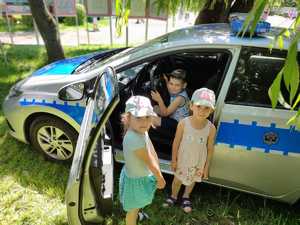 zdjęcie kolorowe: policyjny radiowóz i chłopczyk siedzący na fotelu kierowcy, obok stoją dwie dziewczynki