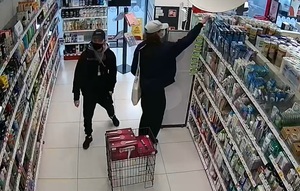 zdjęcie kolorowe; dwóch młodych mężczyzn ubranych w czarne spodnie i bluzy z zasłoniętymi maseczkami ochronnymi twarzami w alejce sklepu kosmetycznego