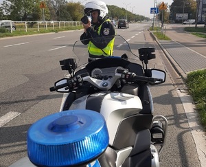 zdjęcie kolorowe: policjant wydziału ruchu drogowego stojący przed motocyklem służbowym z urządzeniem do pomiaru prędkości pojazdów