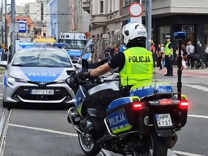 zdjęcie kolorowe:  policjant katowickiej drogówki na motorze służbowych i policyjne radiowozy jadące przed uczestnikami przemarszu.